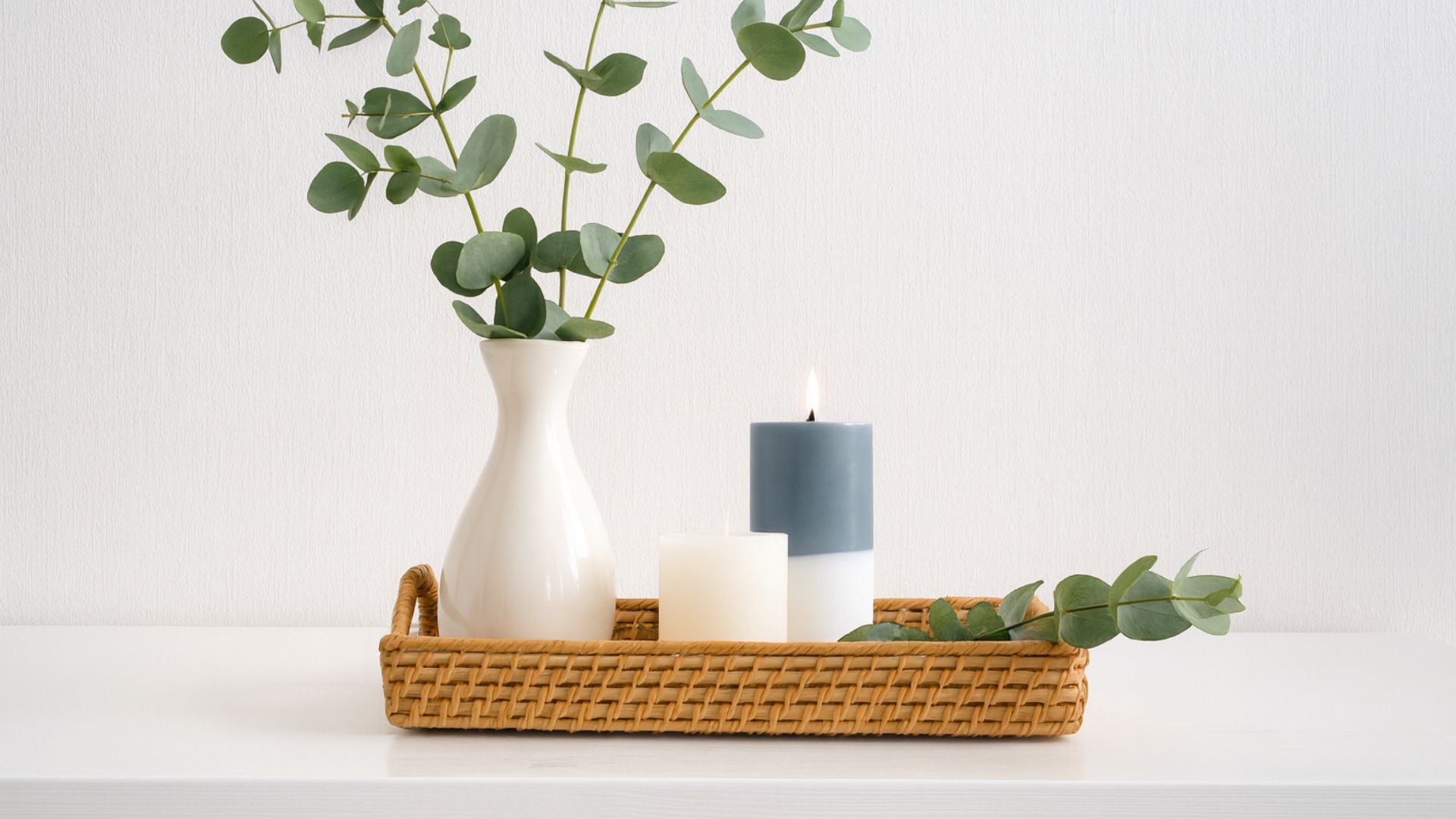 Decorative setup with a vase, candles, and eucalyptus leaves on a white surface.